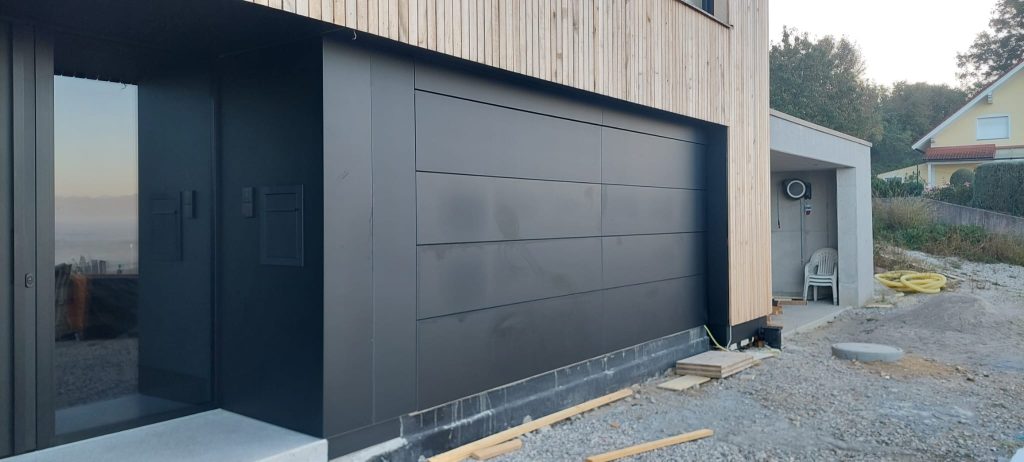 Zeitgemäßes schwarzes Garagentor in glatter Optik, kombiniert mit vertikaler Holzfassade an einem modernen Wohnhaus.