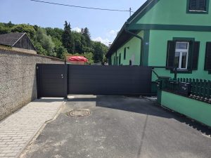 Breites schwarzes Schiebetor aus Aluminium mit integrierter Gartentür, installiert vor einem Wohnhaus von FuMa OG.