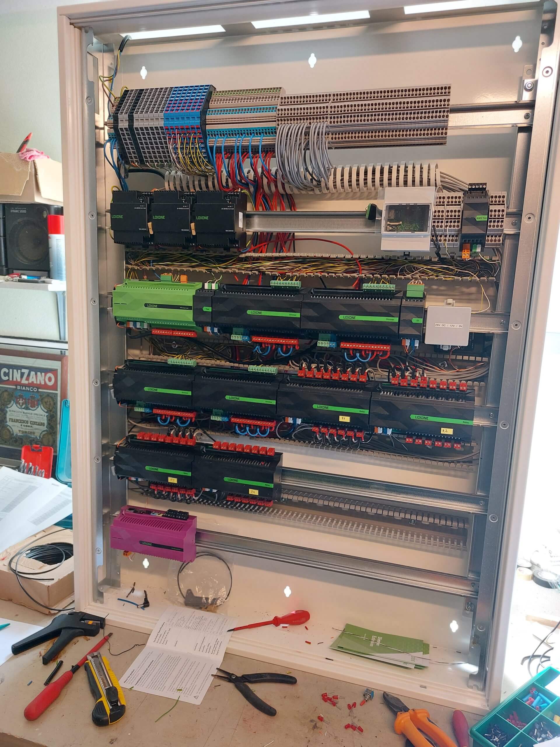 Offener Verteilerkasten mit Loxone Miniserver, Extensions, Reihenklemmen und Werkzeug auf der Werkbank – Elektroinstallation in Arbeit